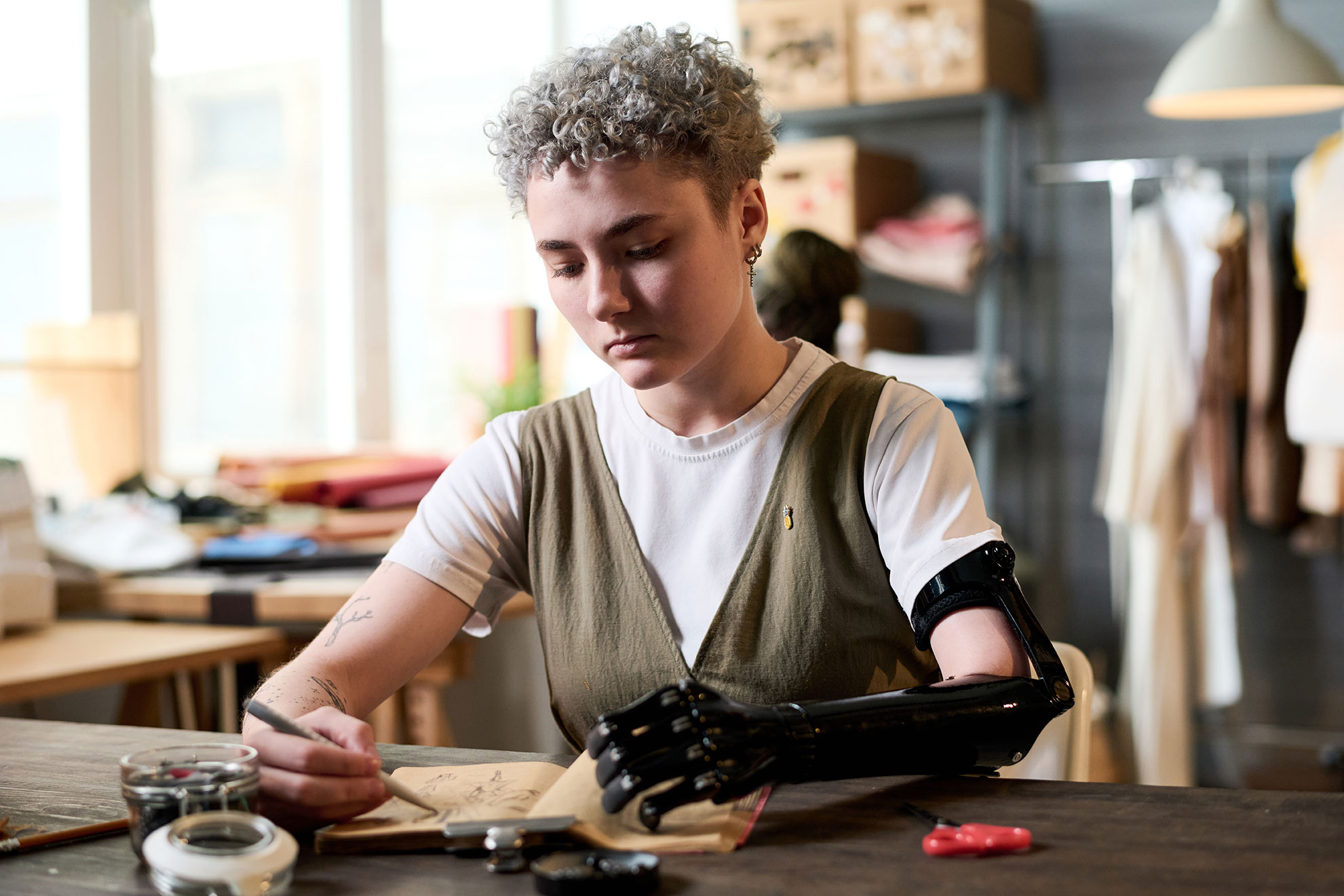 Frau mit Armprothese sitzt an Ihrem Arbeitstisch und schaut in einen Laptop.